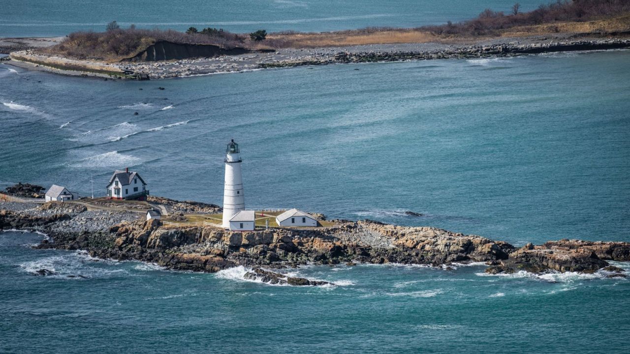 Scenic coastal view of a white lighthouse on a rocky island with calm blue waters.
