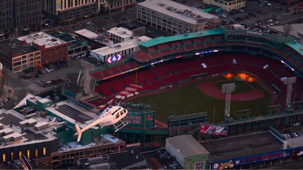 Helicopter flying above Fenway Park with the Boston skyline visible in the distance.