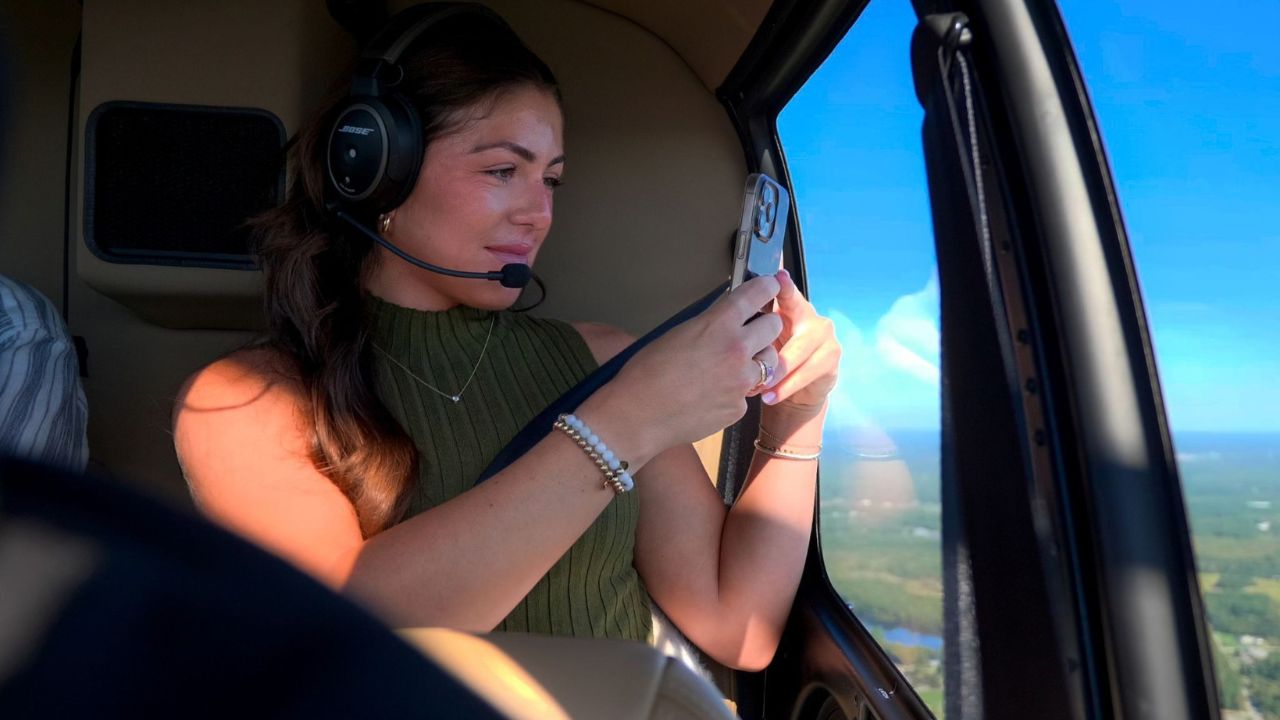  Passenger wearing a headset photographs the view through a private helicopter window during a coastal flight.